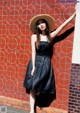 A woman leaning against a red wall wearing a straw hat.