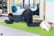 A woman doing a plank on a green mat in a gym.