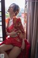 A woman in a red dress sitting by a window.