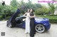 Two women standing next to a blue sports car.