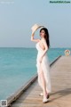 A woman in a white dress and hat standing on a pier.