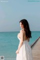 A woman in a white dress standing on a pier by the ocean.