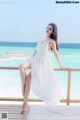 A woman in a white dress sitting on a balcony overlooking the ocean.