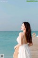 A woman in a white dress standing on a pier by the ocean.