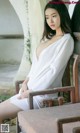 A woman in a white dress sitting on a wooden chair.