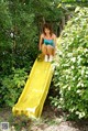 A woman sitting on a yellow slide in the woods.