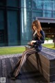 A woman sitting on a wooden bench in front of a building.