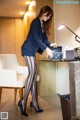 A woman in a business suit and stockings standing in front of a desk.