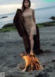 A woman standing next to a fire on a beach.