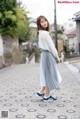 A woman in a white shirt and a gray skirt is walking down a street.