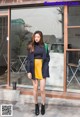 A woman standing in front of a building wearing a yellow skirt.