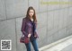 A woman standing in front of a gray wall holding a red bag.