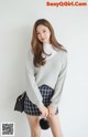 a woman in a gray sweater and plaid skirt posing for a picture