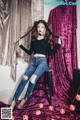 A woman sitting on top of a stool in front of a curtain.