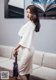 A woman in a white dress standing in front of a couch.