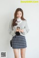 a woman in a gray sweater and plaid skirt holding a cell phone