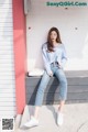 A woman sitting on a bench wearing a blue sweater and jeans.