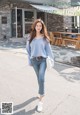 a woman walking down the street wearing a blue sweater and jeans