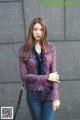 A woman standing in front of a gray wall wearing a red and blue blouse.