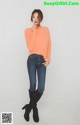 A woman in an orange sweater and jeans posing for a picture.