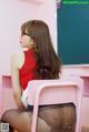 A woman sitting on a pink chair in front of a blackboard.