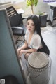 A woman sitting on top of a desk next to a fan.