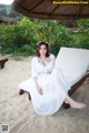 A woman in a white dress sitting on a lounge chair on the beach.