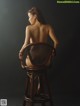 A naked woman sitting on a wooden chair.