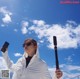 A woman in a white jacket holding a cell phone and a selfie stick.